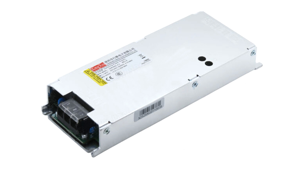 Slim metal AC-DC power supply module with terminal block, mounted flanges, and warning label (angled view). Inlet/outlet area visible at left.